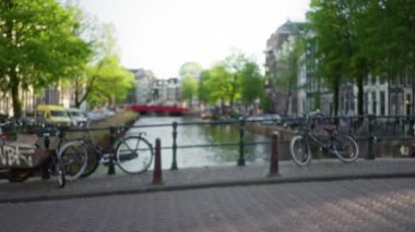 Açık gökyüzünün altında bisiklet, ağaç ve tarihi binaların bulunduğu bulanık kanal sahnesi, baharda Hollanda 'nın özünü yakalıyor..