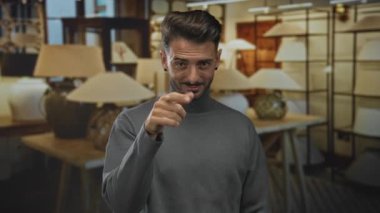 Çağrı jestini modern binadaki bej lambaların arasında parmak kulaklarına kadar gösterir; iletişimi hoş karşılar.