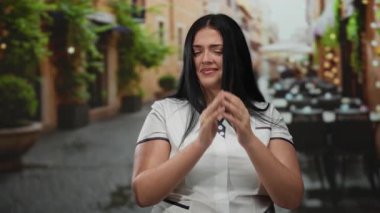 Açık hava restoranının terasında duran bir kadın, atmosferdeki hoş olmayan kokudan rahatsız olmuş gibi görünüyor. Gündüz vakti yemyeşil ve rahat bir ortam var..