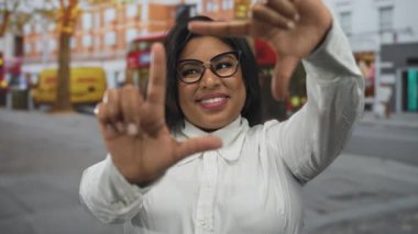 Şehrin sokaklarında gülümseyen bir kadın, sembolik kırmızı otobüslerin ve şehir hayatının arka planına sahip, canlı şehir kültürünü ve çeşitli ifadeleri somutlaştıran bir kare oluşturmak için jestler yapıyor..