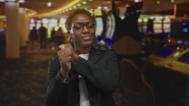 Spor ceket giyen genç Afrikalı Amerikalı kadın gülümserken kumarhane kumar makinelerinde parmaklarını geriye doğru uzattı..