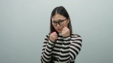 İzole edilmiş beyaz arka plana karşı çizgili süveter giymiş bir kadın. Güç ve stili sembolize eden daracık yumruklar ve gözlüklerle odaklanıyor..