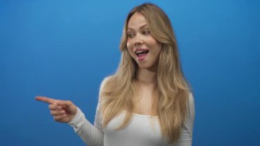 Parlak mavi fotoğraf stüdyosunda işaret parmağı takan sarışın bir kadın. Eğlenceli bir davet..