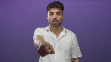 Beyaz gömlek giyen İspanyol genç adam mor stüdyoda parmağını işaret ediyor ve odaklanmış bir ifadeyle;.