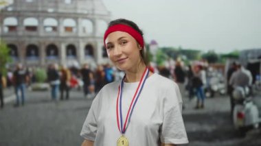 Roma 'nın ikonik kolezyumunun önünde altın madalya ve kırmızı saç bandı takmış, canlı bir açık hava sahnesiyle çevrili, başarı ve neşe duygularını ifade eden bir kadın..