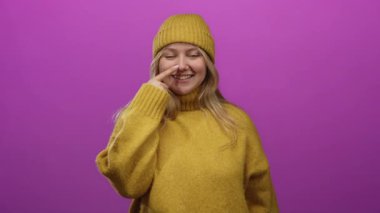 Hardal süveter giyen ve bereli bir kadın burnuna dokunuyor canlı pembe bir fon, neşeli bir cazibe ve sıcaklıkla basit bir stüdyo ortamında yayılıyor..