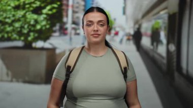 Kendine güveni olan genç bir kadın, arka planda yeşillik olan hareketli bir şehir caddesinde yemin ediyor. Şehir hayatının ortasında kararlılığını gösteriyor..