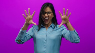 Mavi gömlekli kadın, canlı pembe bir arka plana karşı heyecanla el kol hareketi yapıyor. Enerjisini ve coşkusunu yumrukları havada ve neşeli bir ifadeyle aktarıyor..