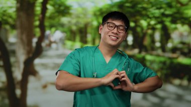 Steteskoplu yeşil elbiseli genç Çinli adam Sunny Park 'ta kalp hareketi yapıyor..