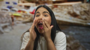 Plajda bağırarak el ele tutuşan genç Latin kökenli kadın, deniz kenarına dönüp arkadaş arıyor..