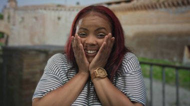 Eski şehir sokağında güneş ışığı altında, yıpranmış tuğla cephede yanakları bastıran bir kadın. Sürpriz..