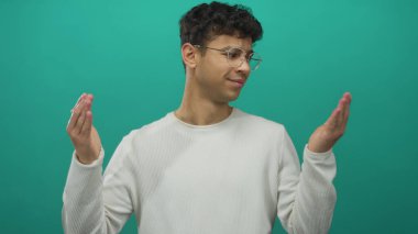 Gözlüklü ve beyaz tişörtlü bir adam, bir sette şaşkın bir ifadeyle omuz silkiyor; belirsizlik.