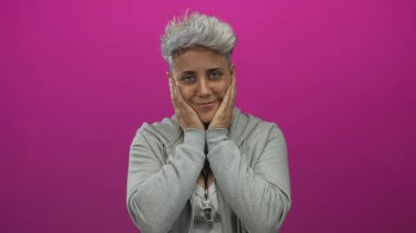 Bir kadın pembe stüdyo ortamında iki eliyle yüzünü diş ağrısı için bastırırken yanaklarını tutuyor; belirsizlik.