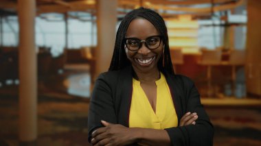 Otel odasında gülümseyen, gözlüklü, sarı gömlekli, sıcak ve neşe saçan bir kadın..