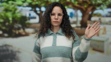 Parkta gözlüklü ve çizgili süveter giyen, güneşli bir günde ağaçlarla çevrili, rahat bir ortamda güneşli bir anı canlandıran bir kadın..