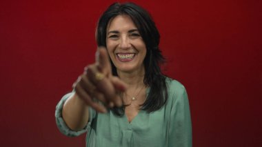 Stüdyoda gülümseyen ve kamerayı işaret eden orta yaşlı İspanyol kadın, neşe ve kahkaha.