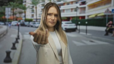 Kalabalık bir caddede el kol gezen genç sarışın bir kadın. Arka planda binalar ve arabalar var. Açık bir şehir ortamında el çabukluğu ve etkileşime işaret ediyor ve davet ediyor.