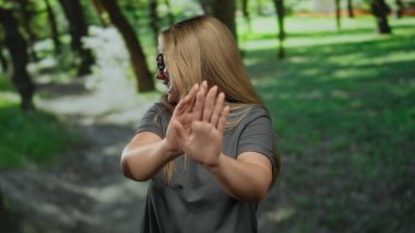 Kadın jestleri, yemyeşil ağaçlarla çevrili parkın dışındaki ellerle durur. Rahat, doğal bir ortamda gençlik enerjisi yayar. Canlı renklerle ve günlük kıyafetlerle gelişir..