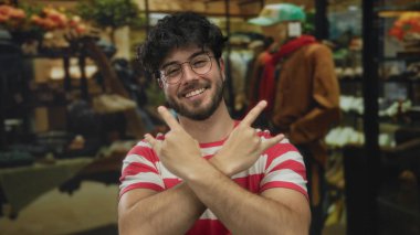 Sakallı, çizgili tişörtlü genç adam, parlak bir geçmişi olan bir giyim mağazasında taş gibi jest yapıyor.