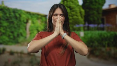 Serin bir park ortamında meditasyon yapan bir kadın, yemyeşil ağaçlar ve canlı yeşilliklerle çevrili, dua ederek sükunetini ifade ediyor..