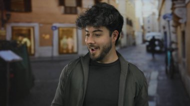 Sakallı genç adam açık gökyüzünün altında mutlu bir şekilde gülerek Avrupa caddesinde eğleniyor.