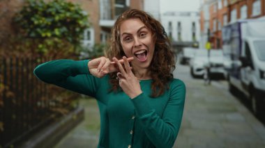 Şehirli şehir sokaklarında hashtag sembolü taşıyan bir kadın, yeşil kazak giyiyor, enerjik bir şekilde gülümsüyor, sosyal medyayı ve yaşam tarzını ön plana çıkarıyor..