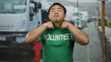 Şehir sokağında yeşil gönüllü gömleği ayarlayan genç bir adam. Arka planda kamyonları var. Gönüllü işine ve kamu hizmetine olan güveni ve gururu tam..
