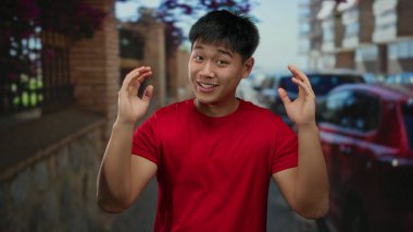 Kırmızı gömlekli genç adam şehir sokaklarında büyük bir jest yapıyor. Arka planda arabaları var. Heyecan ve nişan gösterisi yapıyorlar..