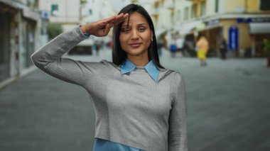 Kadın, hareketli bir sokakta kendine güvenle selamlıyor zarafeti günlük tarzla harmanlıyor şehir cazibesini ve profesyonelliği canlı sokak hayatı zarafetle gözler önüne seriyor..