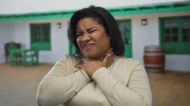 Şehrin açık bir caddesinde acı dolu bir ifadeyle duran ve yeşil aksanlı beyaz bir binanın önünde bej bir bluz giyen bir kadın..