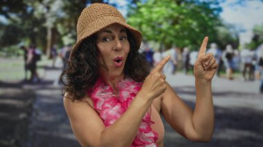 Orta yaşlı İspanyol kadın, bikini şapkası takıyor ve her iki parmağıyla parkı işaret ediyor; yaz tatili..