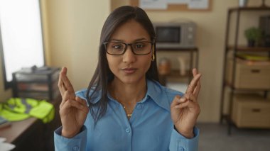Ofiste gözlüklü bir kadın iş ortamında umudunu ifade ederek kapalı bir ortamda konsantrasyon ve beklenti içinde..