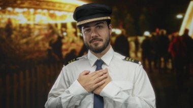 Işıl ışıl gülümseyen bir tebessümle genç İspanyol bir adam coşkulu bir gece fuarında elleri kalbimde duruyor. Minnettarlığın ve sevincin iç açıcı bir görüntüsünü oluşturuyor..