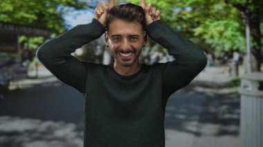 İşaret parmağını yukarı doğru gösteren adam yeşil ağaçlar ve bulanık şehir yaprakları ile aynı hizada. Keyif doğallığı eğlence oyunculuğu..