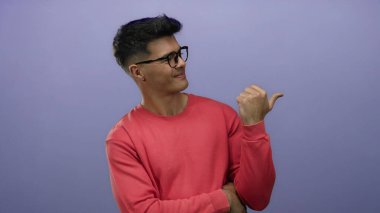 Gözlüklü ve kırmızı gömlekli genç adam mor arka planda duruyor. Ayrı bir ortamda başparmak hareketlerini güven ve cazibeyle gösteriyor.