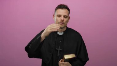 Pembe arka planda İncil 'i tutan ve alnına dokunan bir rahip.