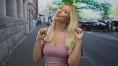 Pembe bluzlu sarışın kadın şehir sokaklarında elleri ağaçlı ve araçlı elleriyle pençe hareketi yapıyor; kendini ifade etme sevinci.