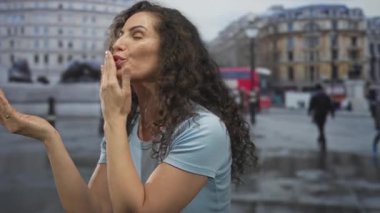 Islak bir kaldırım taşı meydanında yoldan geçenlere el kaldırarak öpücük yollayan bir kadın..