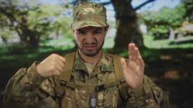 Kamuflaj üniformalı genç İspanyol adam, yeşil orman manzarasının ortasında göğsüne yakın el ele tutuşuyor..