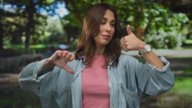 Neşeli bir açık hava parkı ortamında olumlu ve olumsuz duyguları ifade eden bir kadın. Karışık duygular, bir gülümseme ve güneş ışığı altında düşünceli bir ifade sergiliyor..