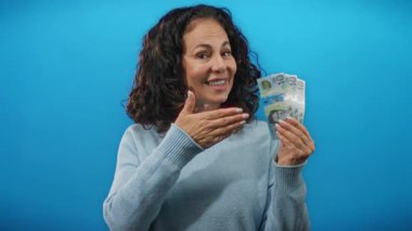 Gülümseyen kadın, Avustralya dolarlarını tutuyor. Mavi duvara başparmak işareti yapıyor. Finansal başarı fikrini gösteriyor..