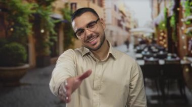 Gözlüklü genç İspanyol adam, sokakta el sıkışarak gülümsüyor, arkadaşlığı selamlıyor..