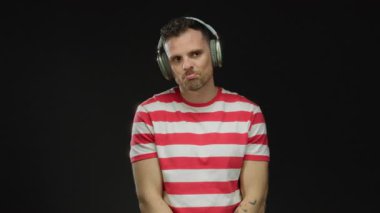 Kulaklıklı genç bir adam siyah bir arkaplana karşı çizgili gömlek giyiyor. Düşünceli bir ifadeyle rahatlamış bir ruh hali ve şık bir moda anlayışının altını çiziyor.