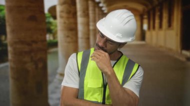 Beyaz kasketli ve yelekli bir adam eski kasaba sokaklarında taş sütunlarla yumruk yumruğa öksürüyor..