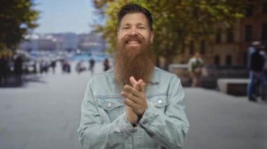 Yoğun şehir caddesinde gün içinde el çırpan, sakallı ve kot ceket giyen bir adam, yayalar arkasında belirsizleşti; mutluluk.