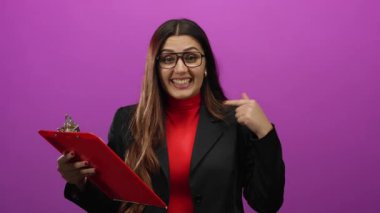 Gözlüklü İspanyol kadın, emsalsiz pembe arka planda kendine güvenen kırmızı bir pano tutuyor, güçlendirme ve profesyonelliği somutlaştırıyor..