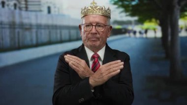 Kıdemli adam, taç ve takım elbise giyip sokakta dikiliyor, kollarını kavuşturup, iş kıyafetlerini mizahi kraliyet imajıyla harmanlıyor..