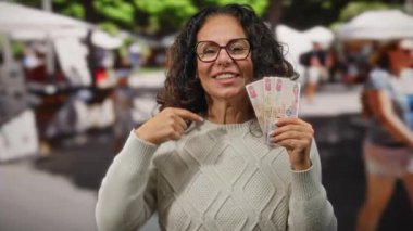 Birleşik Arap Emirlikleri 'nin bir şehrinde orta yaşlı bir kadın gülümseyip dişlerini gösterirken dirhem banknotları gösteriyor..