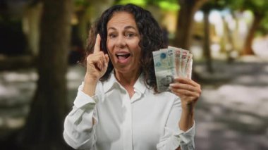 Şehir sokaklarında orta yaşlı bir kadın, İngiliz banknotlarını düşünceli bir ifadeyle elinde tutuyor. Şehir ortamında finansal bir fikri sembolize ediyor..