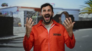 Turuncu hapishane tulumlu İspanyol bir adam sokakta dikiliyor, bir binanın arka planına karşı şaşkınlık ve duygularını ifade ediyor..